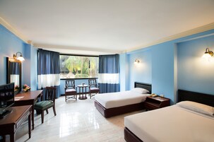 Quarto de hotel com duas camas, uma escrivaninha com cadeira, televisão e janela com cortinas.