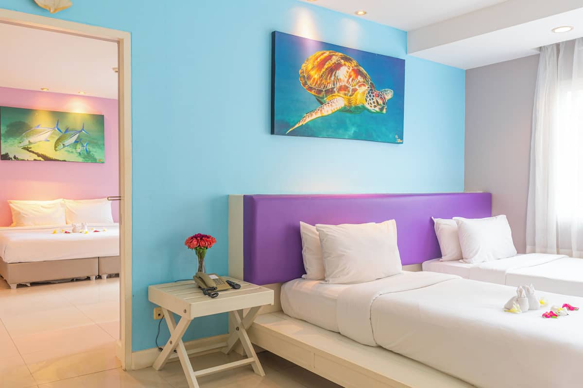A hotel room with a bed, a desk with a phone, a painting of a sea turtle, and a window with curtains.