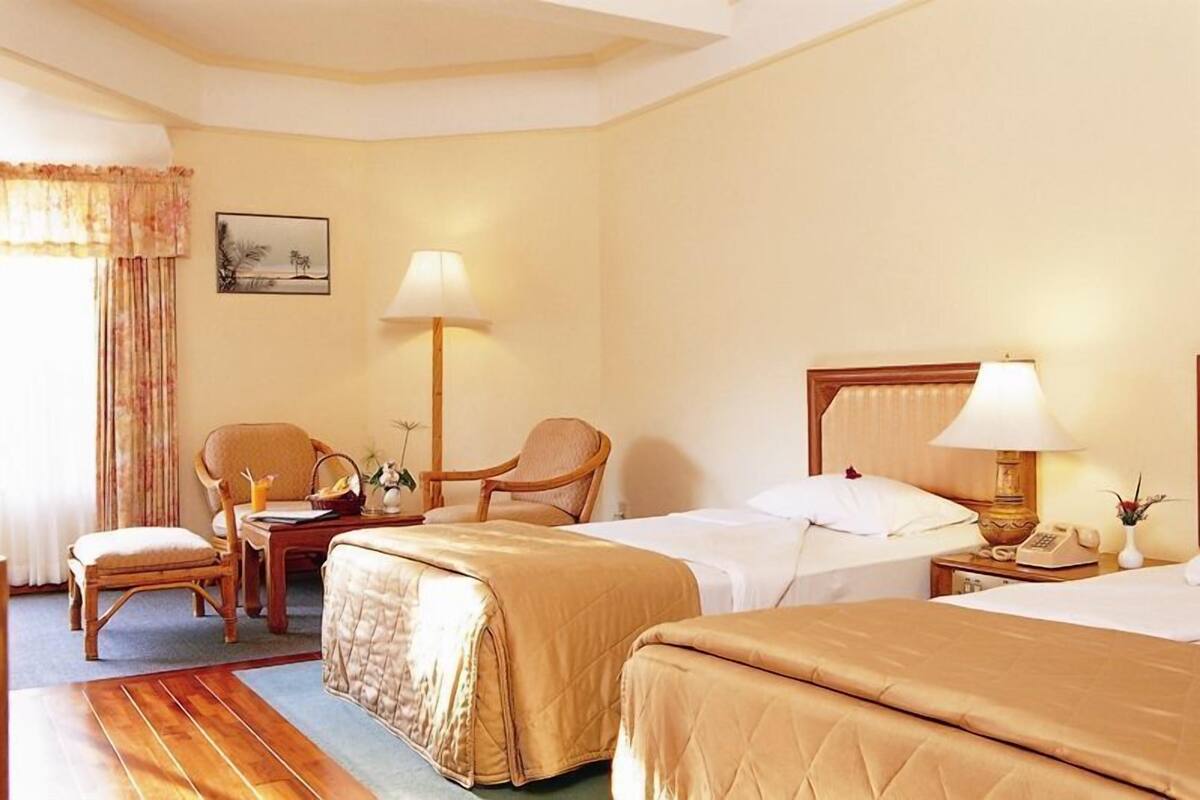 A hotel room with two beds, a desk with a lamp, a chair, and a nightstand with a phone.