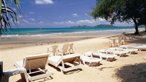 Una playa con filas de sillas reclinables blancas y una palmera.