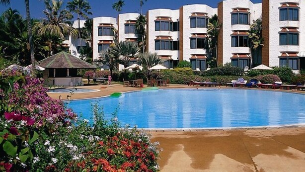 Un hotel con piscina, palmeras y un cielo azul despejado.