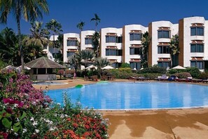 Un hotel con piscina, palmeras y un cielo azul despejado.