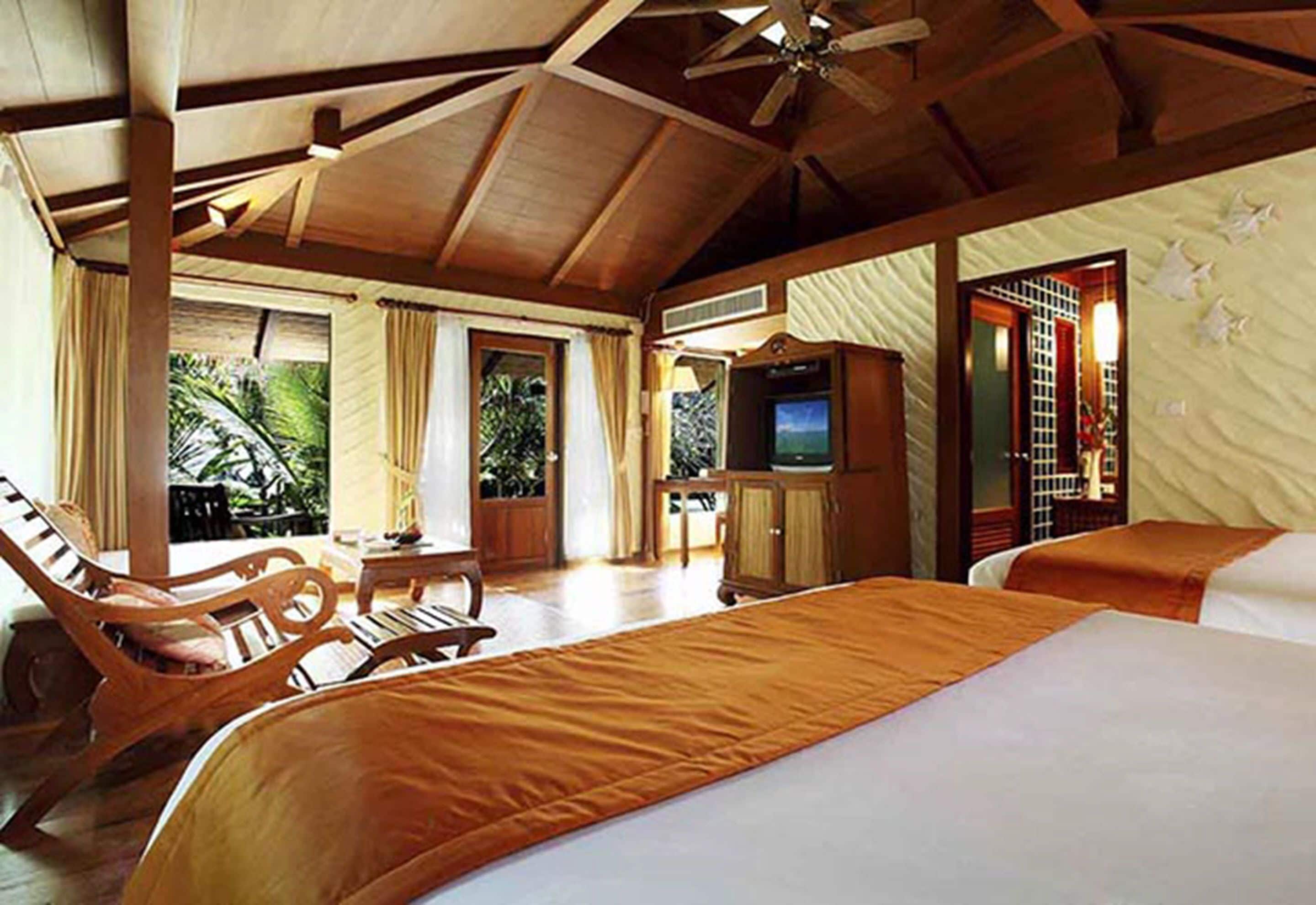 A spacious bedroom with a large bed, wooden furniture, a television, and a view of the outdoors.