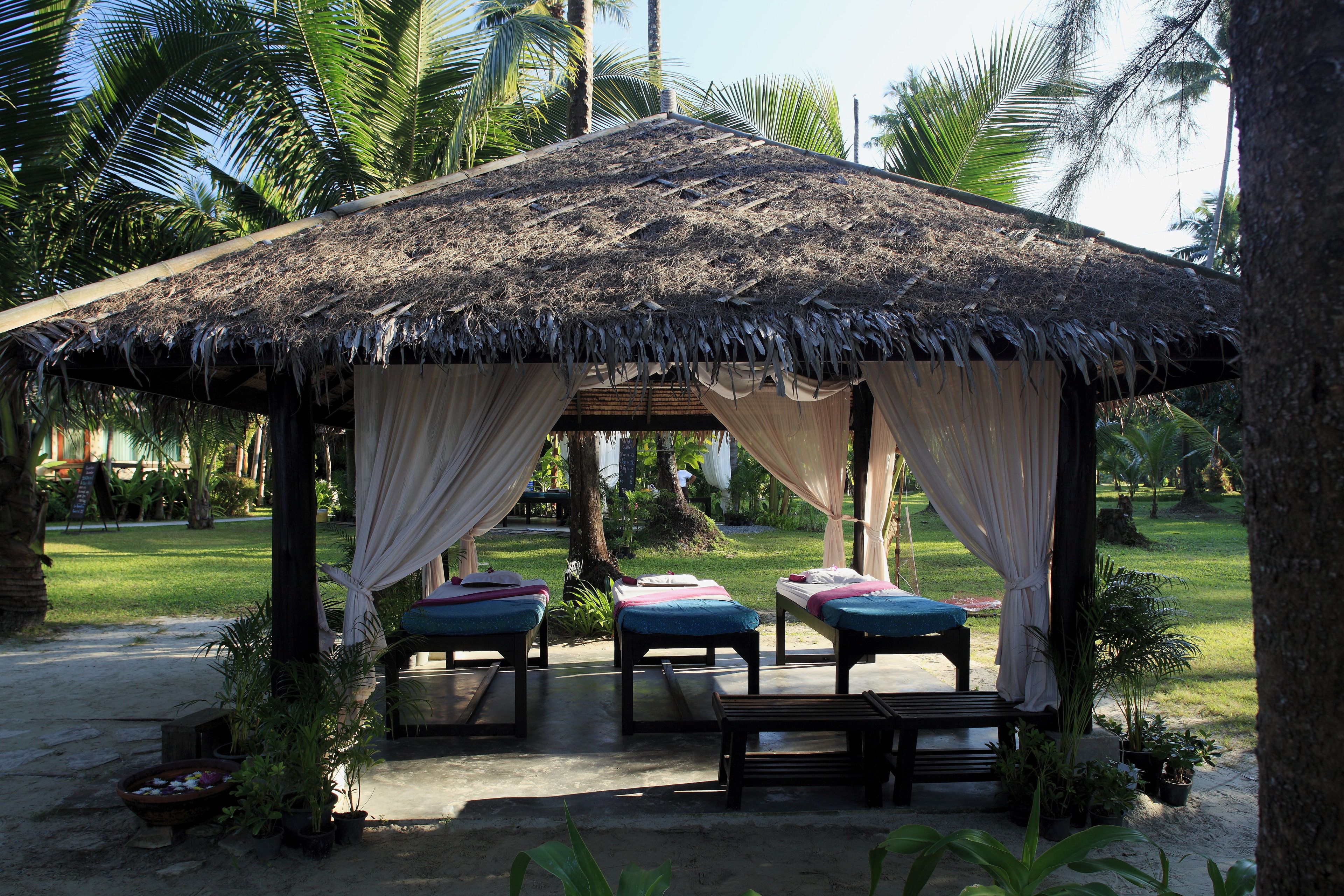A thatched-roof structure with three massage tables, each with a cushion and a towel.