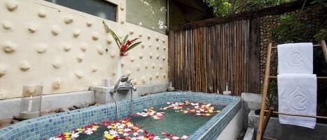 Un área de spa con un jacuzzi revestido de azulejos, rodeado por una pared de piedra y una cerca de madera.