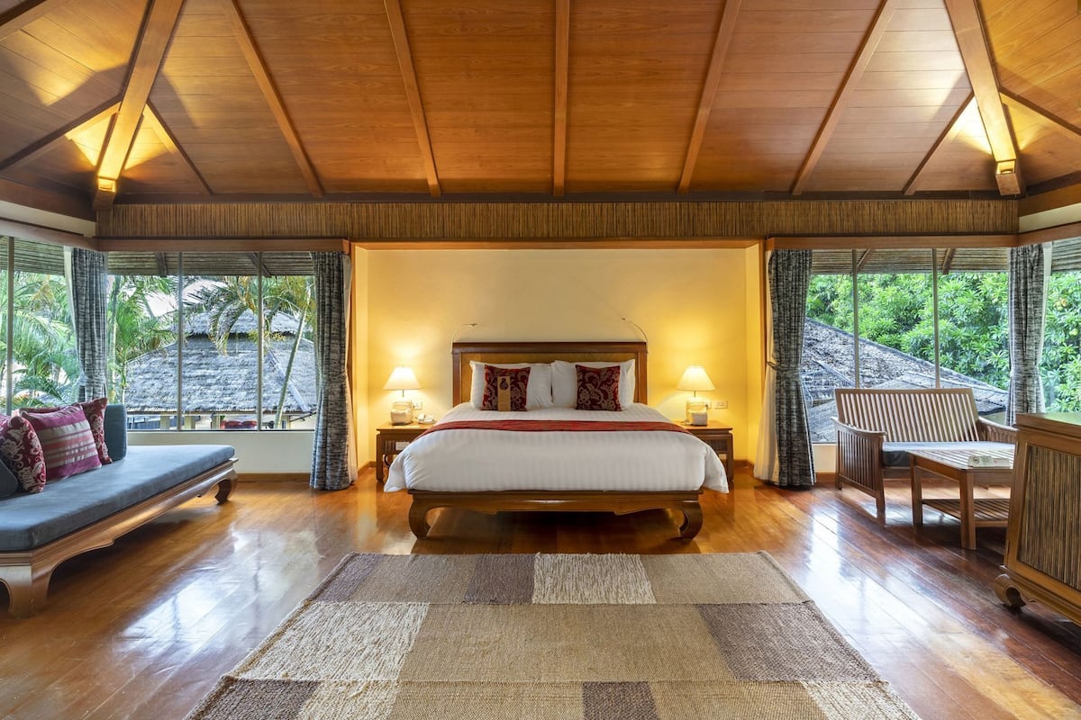 Een ruime slaapkamer met een groot bed, houten balken in het plafond, uitzicht op de omgeving, een zithoek en een nachtkastje met lamp.