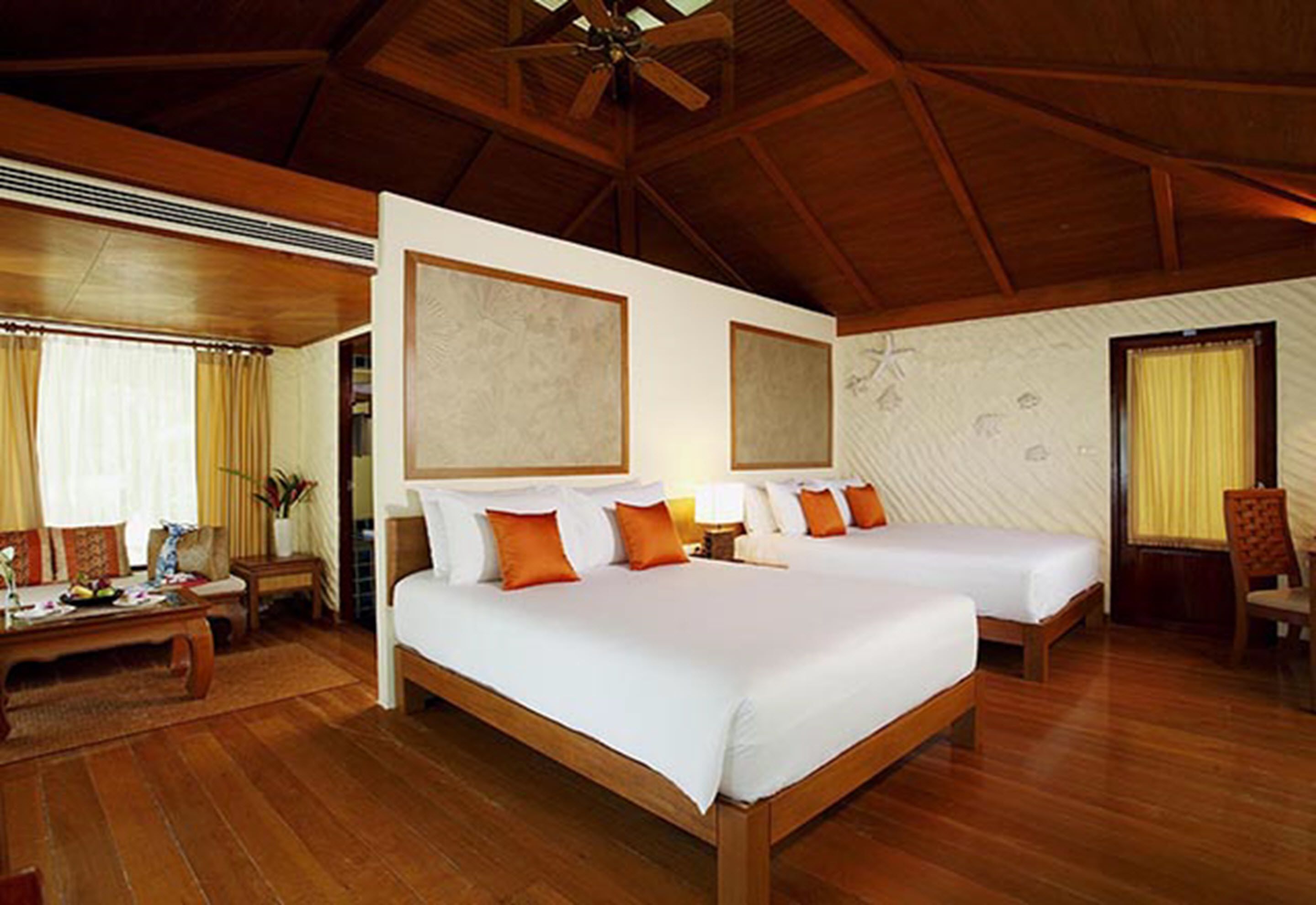A hotel room with two beds, wooden flooring, a ceiling fan, and a large window with curtains.