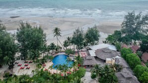Een resort met een zwembad, omringd door palmbomen en ligbedden, met uitzicht op de zee.