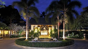 A resort with a well-lit entrance, palm trees, and a fountain.