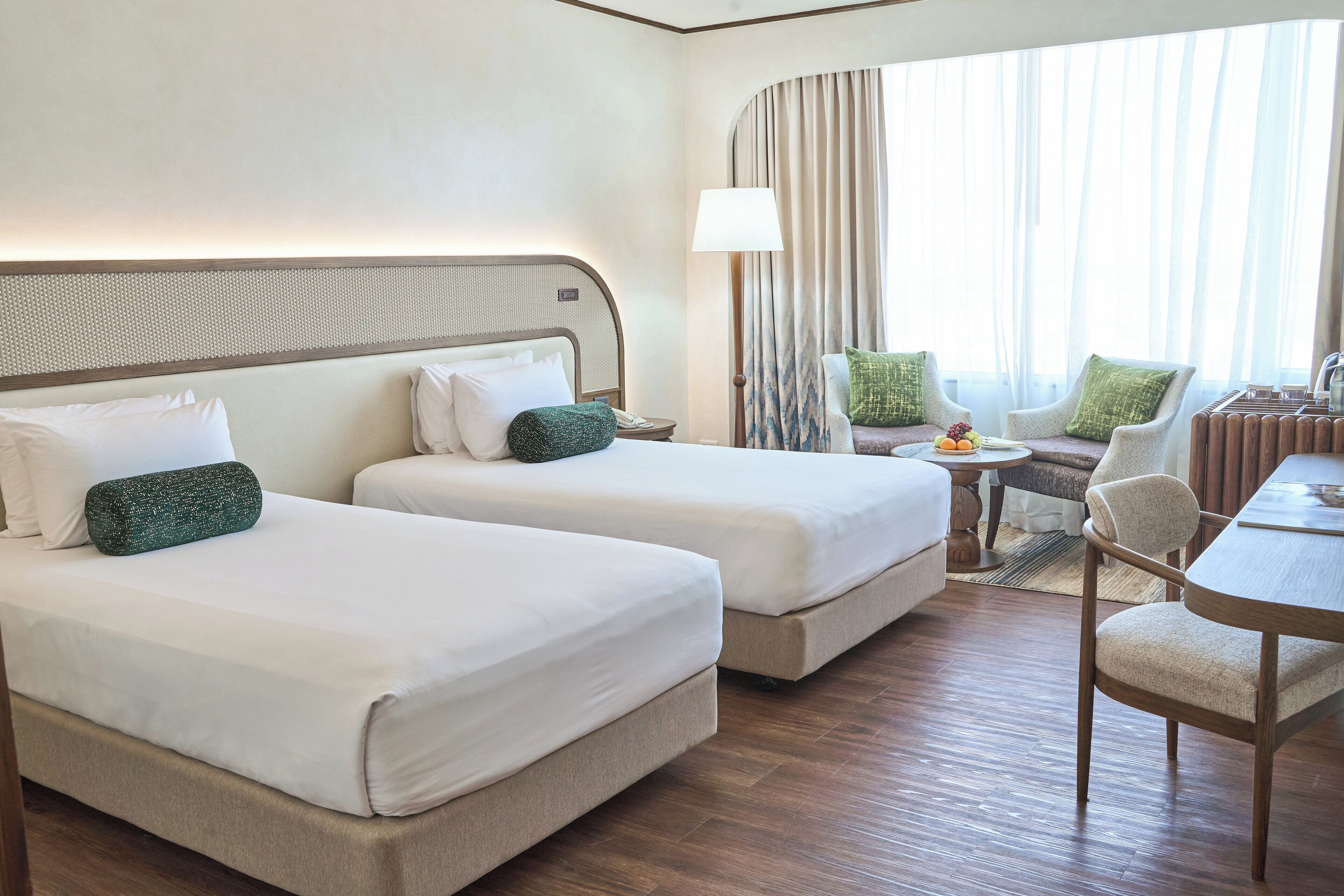 Habitación de hotel con dos camas, una mesita, una silla y vistas al exterior.