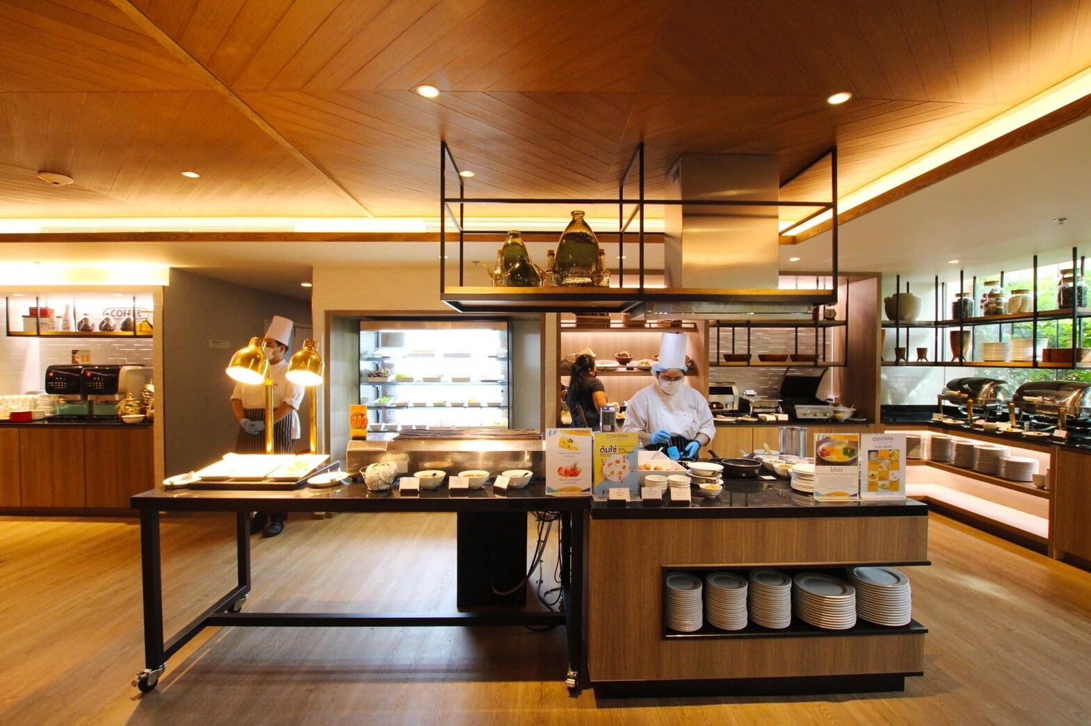 A modern restaurant interior with chefs preparing food, a buffet counter, and a coffee station.