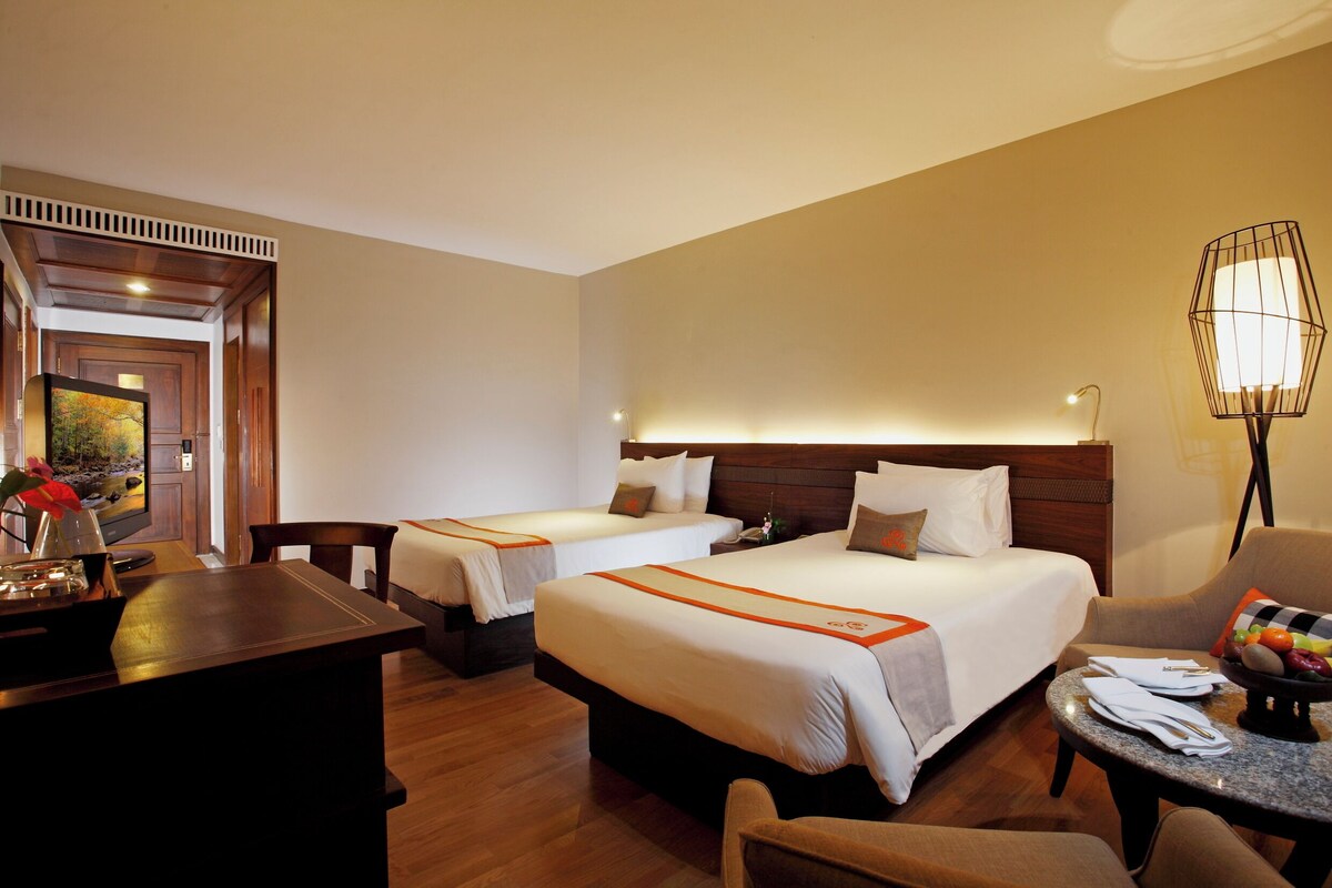 Une chambre d’hôtel avec deux lits, un bureau, une chaise, une petite table et une lampe.