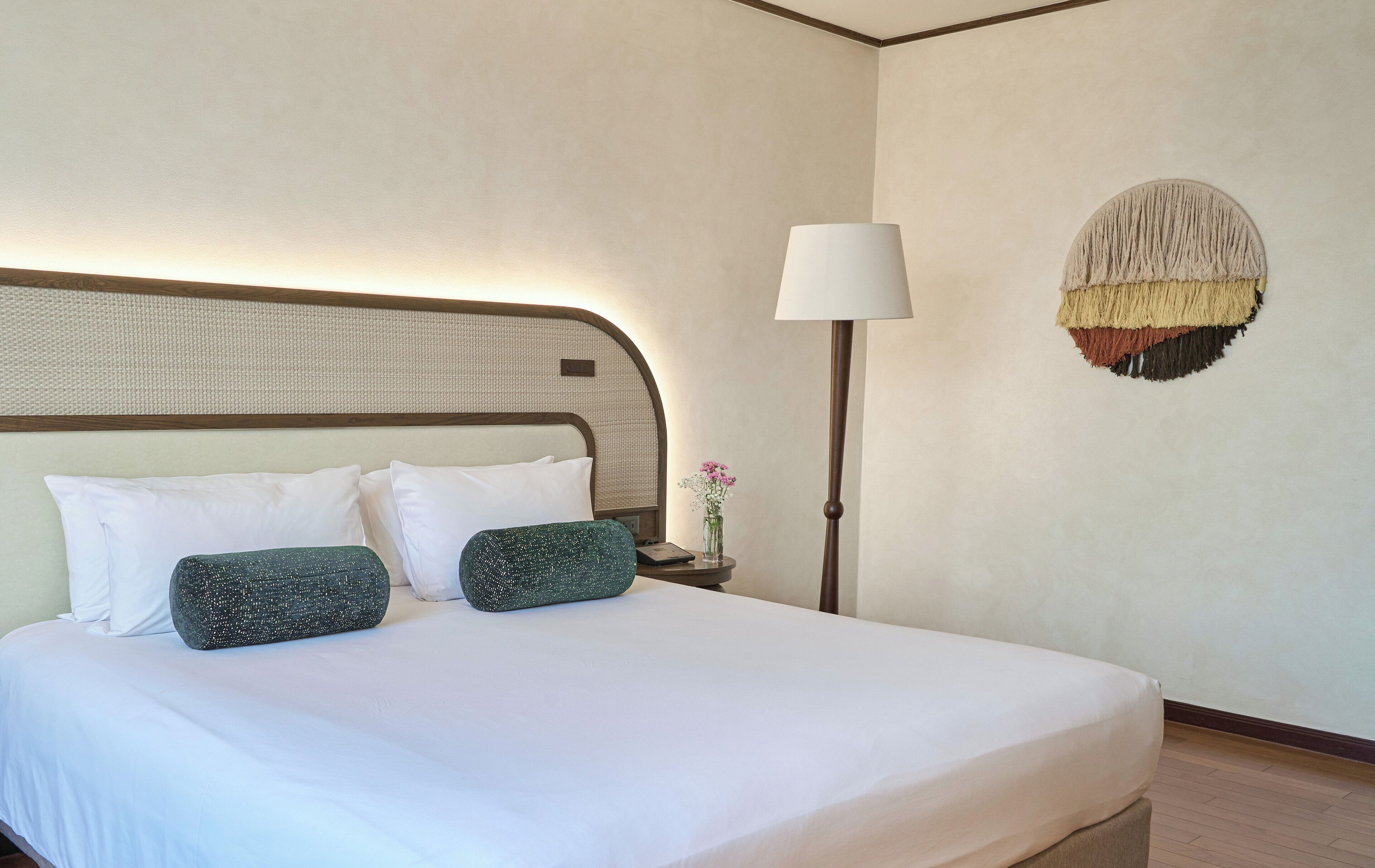 A neatly made bed with white and green pillows, a bedside lamp, and a wall-mounted decorative piece.