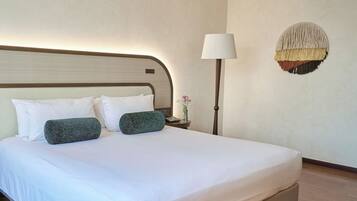 A neatly made bed with white and green pillows, a bedside lamp, and a wall-mounted decorative piece.