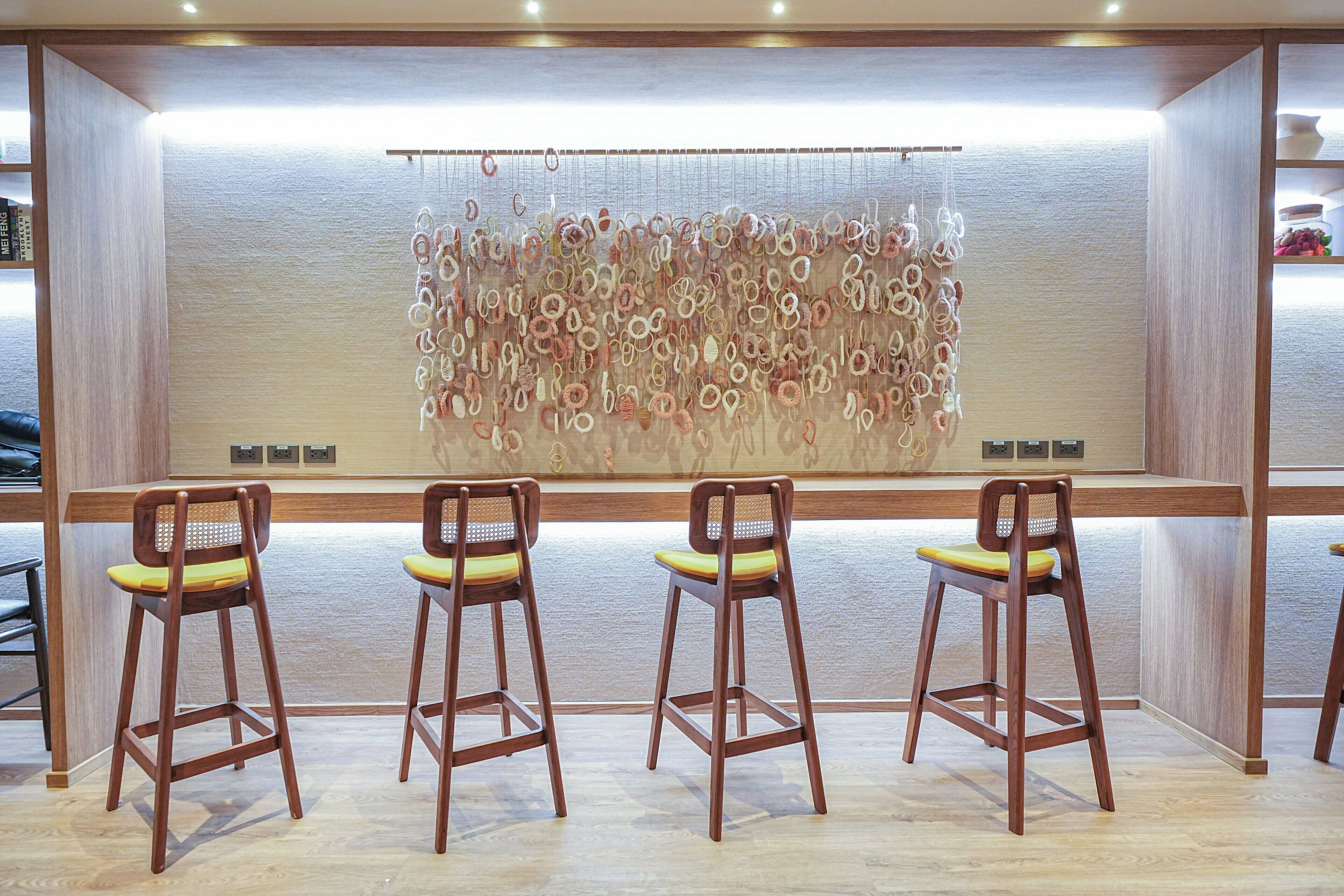 A bar area with three wooden bar stools and a decorative wall hanging.