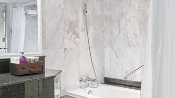 Un baño moderno con pared de mármol, una bañera, una ducha con cabezal de ducha manual, un tocador con dispensador de jabón y un espejo.