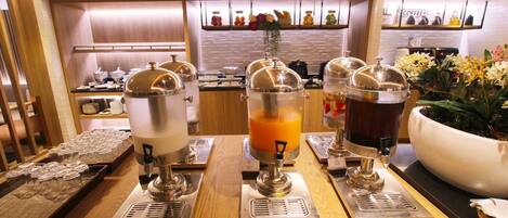 A breakfast bar with three beverage dispensers, a coffee machine, and a large flower pot.