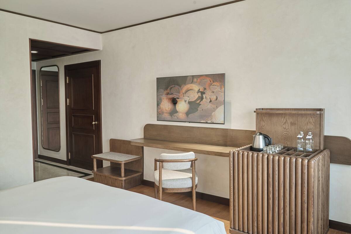 Una habitación de hotel con una cama, un escritorio de madera, una silla y un cuadro en la pared.