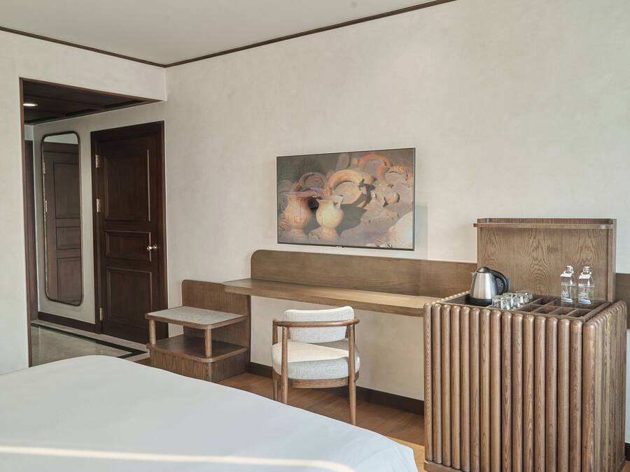 A hotel room with a bed, a wooden desk, a chair, and a painting on the wall.