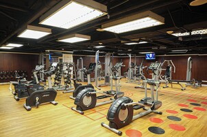 A gym with various exercise equipment, including treadmills and weight machines, arranged on a wooden floor with a patterned design.