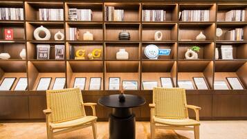 Una biblioteca con estanterías, dos sillones de mimbre, una mesa negra y diplomas en la pared.