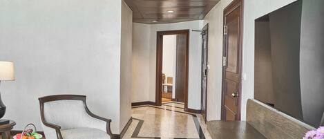 Un vestíbulo de hotel con piso de madera, una zona de estar con una silla, una mesa con revistas y una pantalla de televisión.