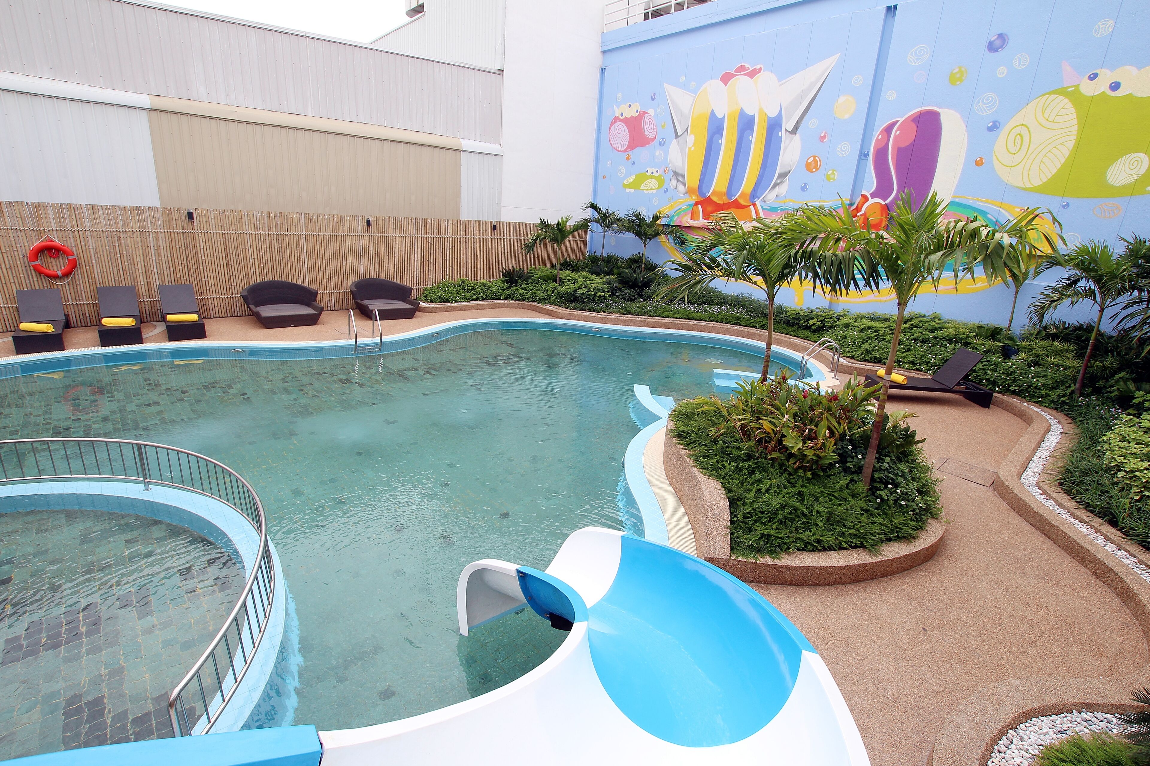 A swimming pool with a slide, lounge chairs, and a mural on the wall.