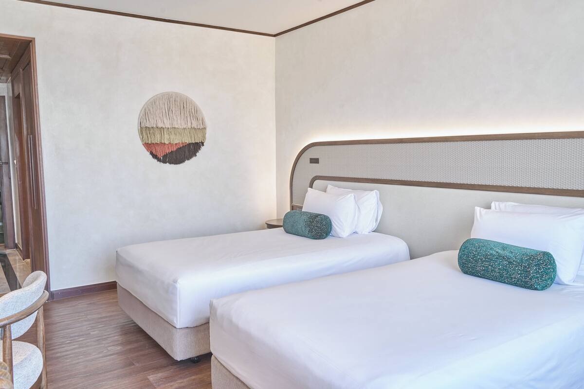 Habitación de hotel con dos camas individuales, un adorno circular en la pared y suelo de madera.