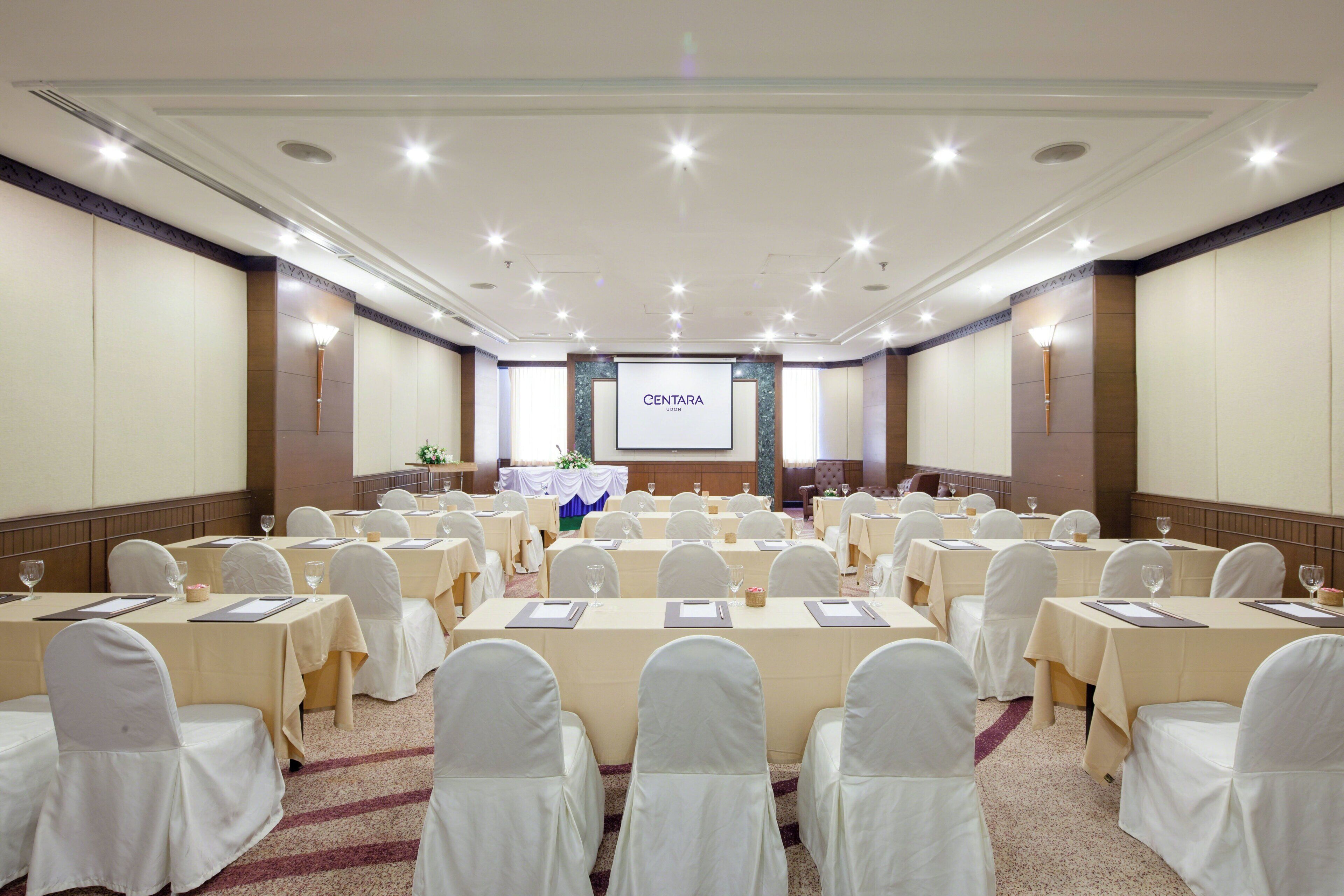 A conference room with multiple tables, white chairs, and a projection screen in the center.