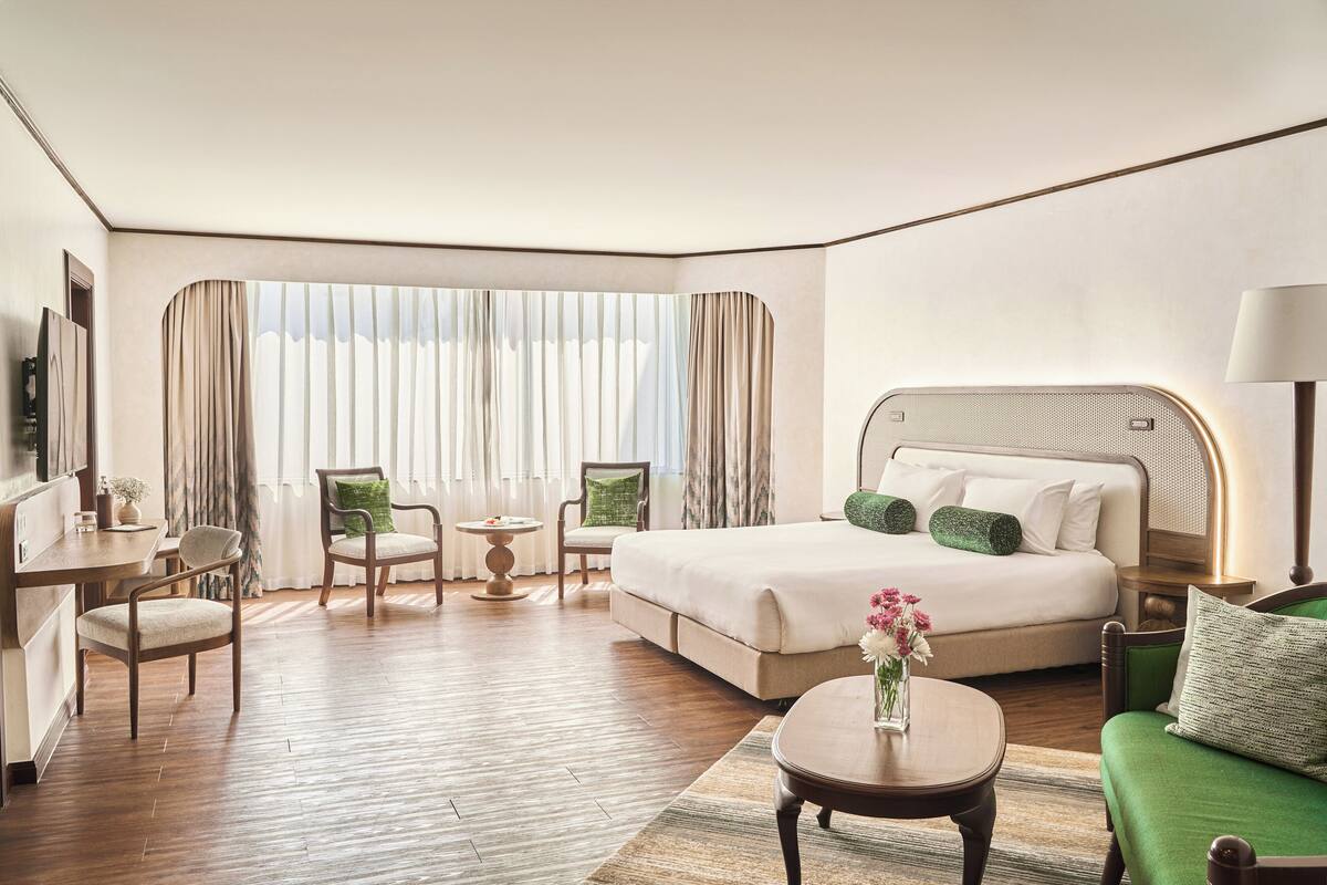 Habitación de hotel con una cama grande, un escritorio, una silla, una mesita pequeña y un sofá verde.