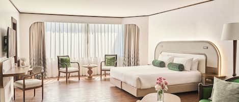 Habitación de hotel con una cama grande, un escritorio, una silla, una mesita pequeña y un sofá verde.