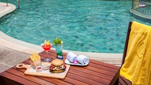 Mesa junto a la piscina con una hamburguesa, papas fritas, una bebida y toallas.