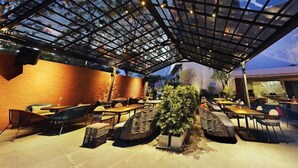 Un espacio al aire libre con mesas y sillas, techo de cristal y pared de ladrillo.