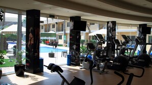 Una palestra con attrezzature per esercizi, ampie finestre e vista su una piscina e edifici esterni.