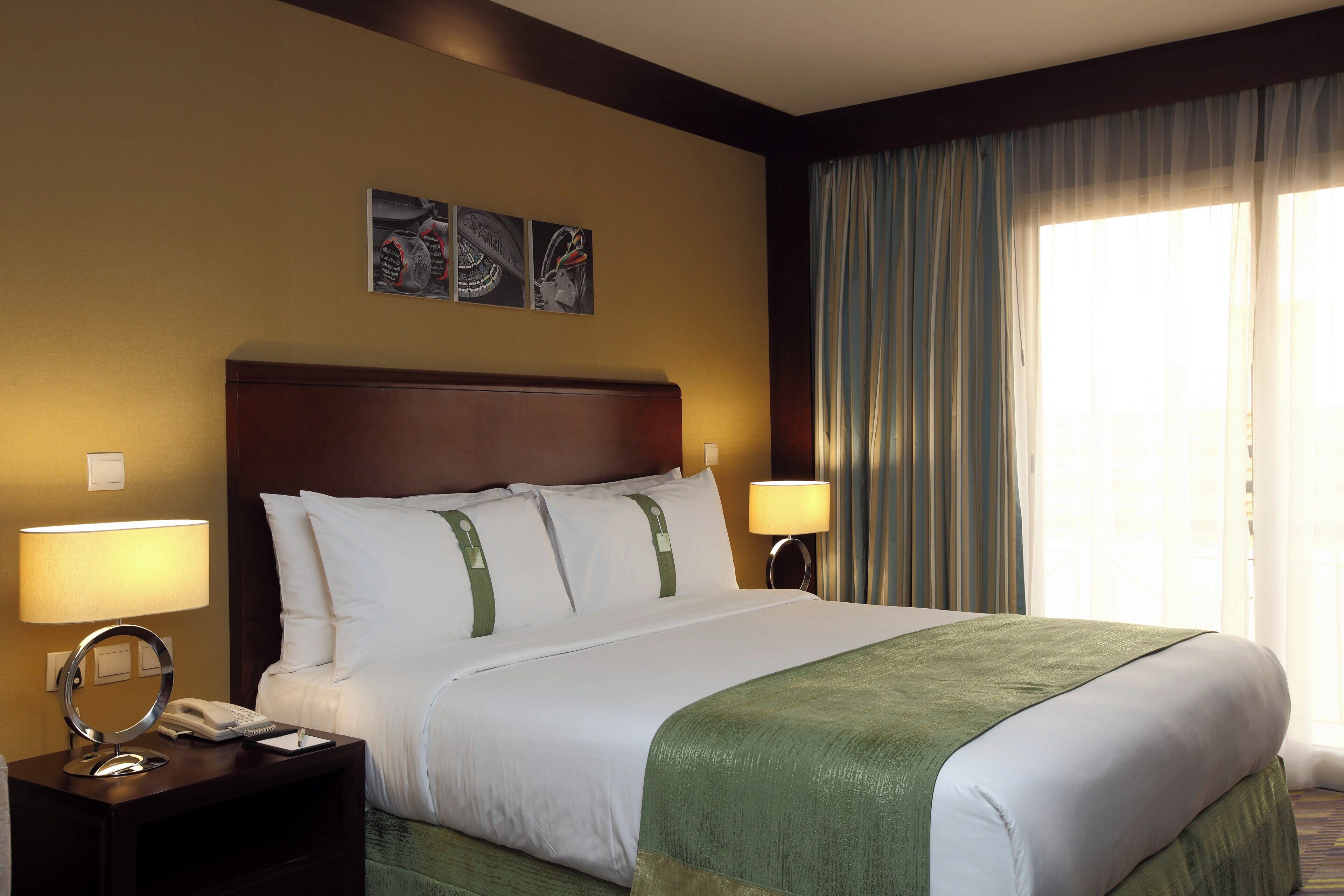 Habitación de hotel con cama, dos lámparas de noche, teléfono y una obra de arte en la pared.