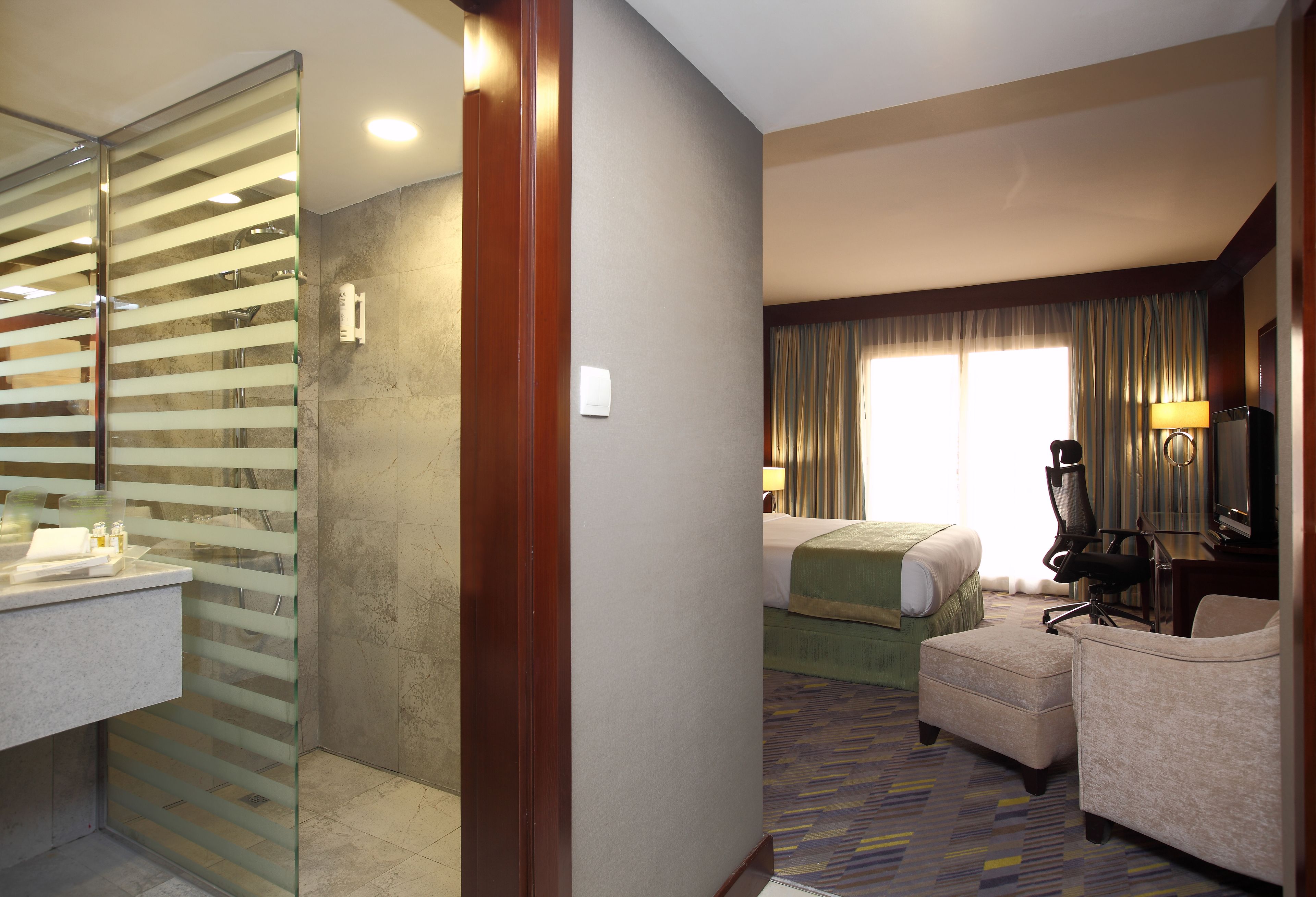 A hotel room with a bathroom, a bed, a desk, and a chair.