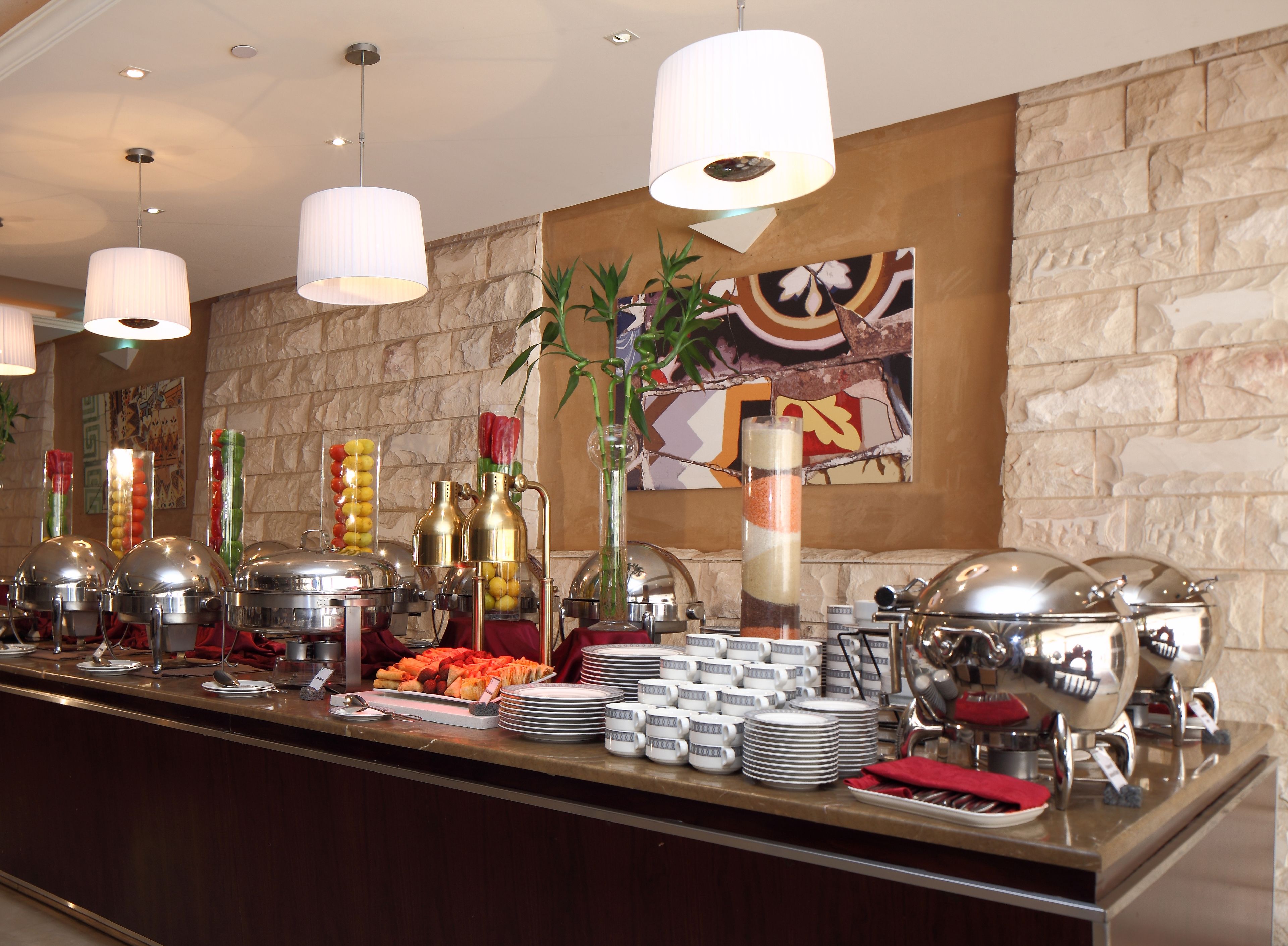 Montaje de bufé con diferentes opciones de comida, recipientes de servicio y una pared decorativa con un cuadro.