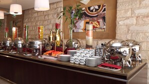 A buffet setup with various food items, serving dishes, and a decorative wall with a painting. - Holiday Inn Al Khobar - Corniche by IHG (Al Khobar)