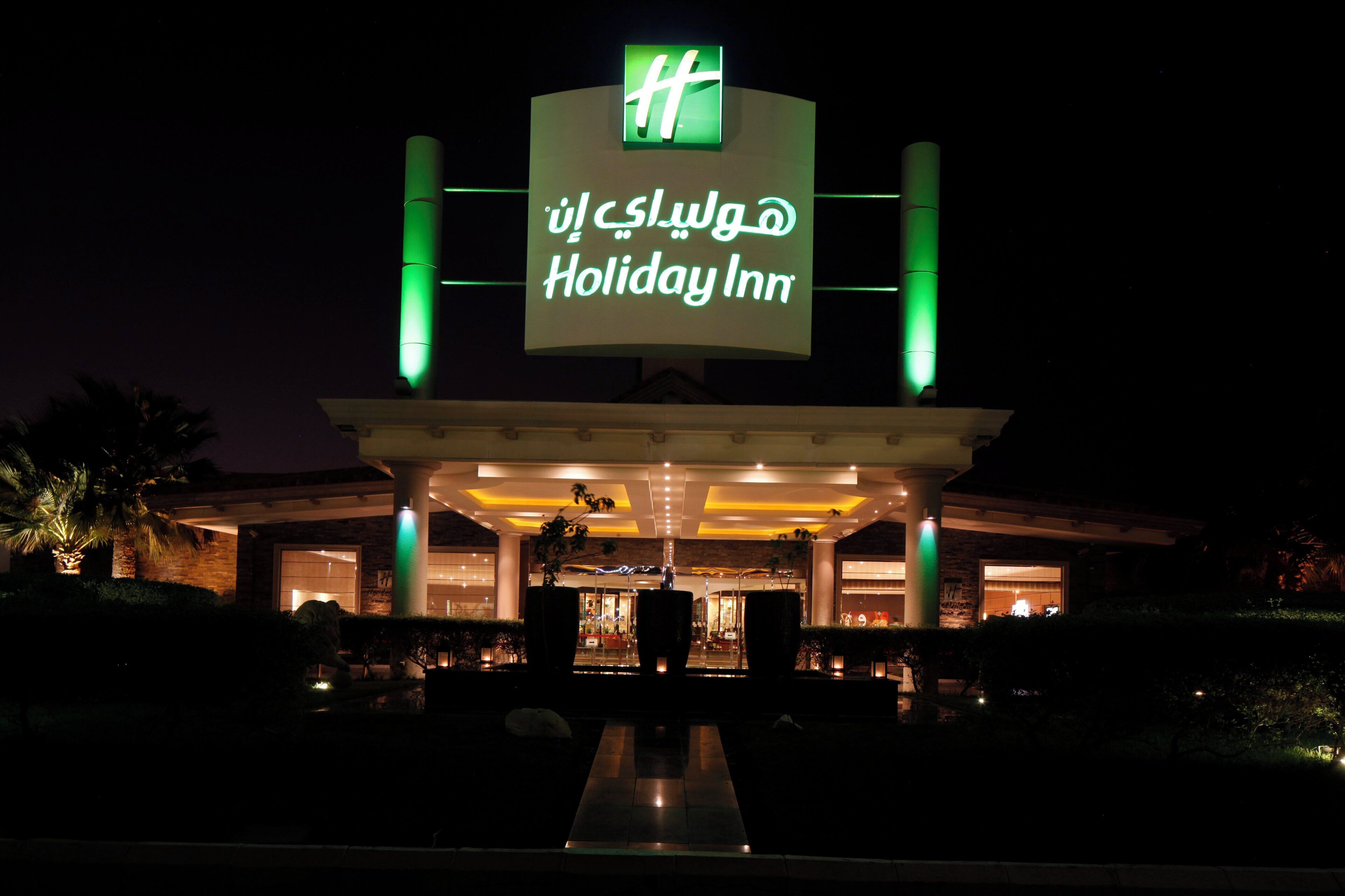 A Holiday Inn sign with a green light, a covered entrance, and a well-lit building facade.