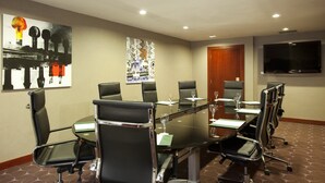 Una sala conferenze con un tavolo in vetro, sedie nere e un grande schermo piatto a parete.