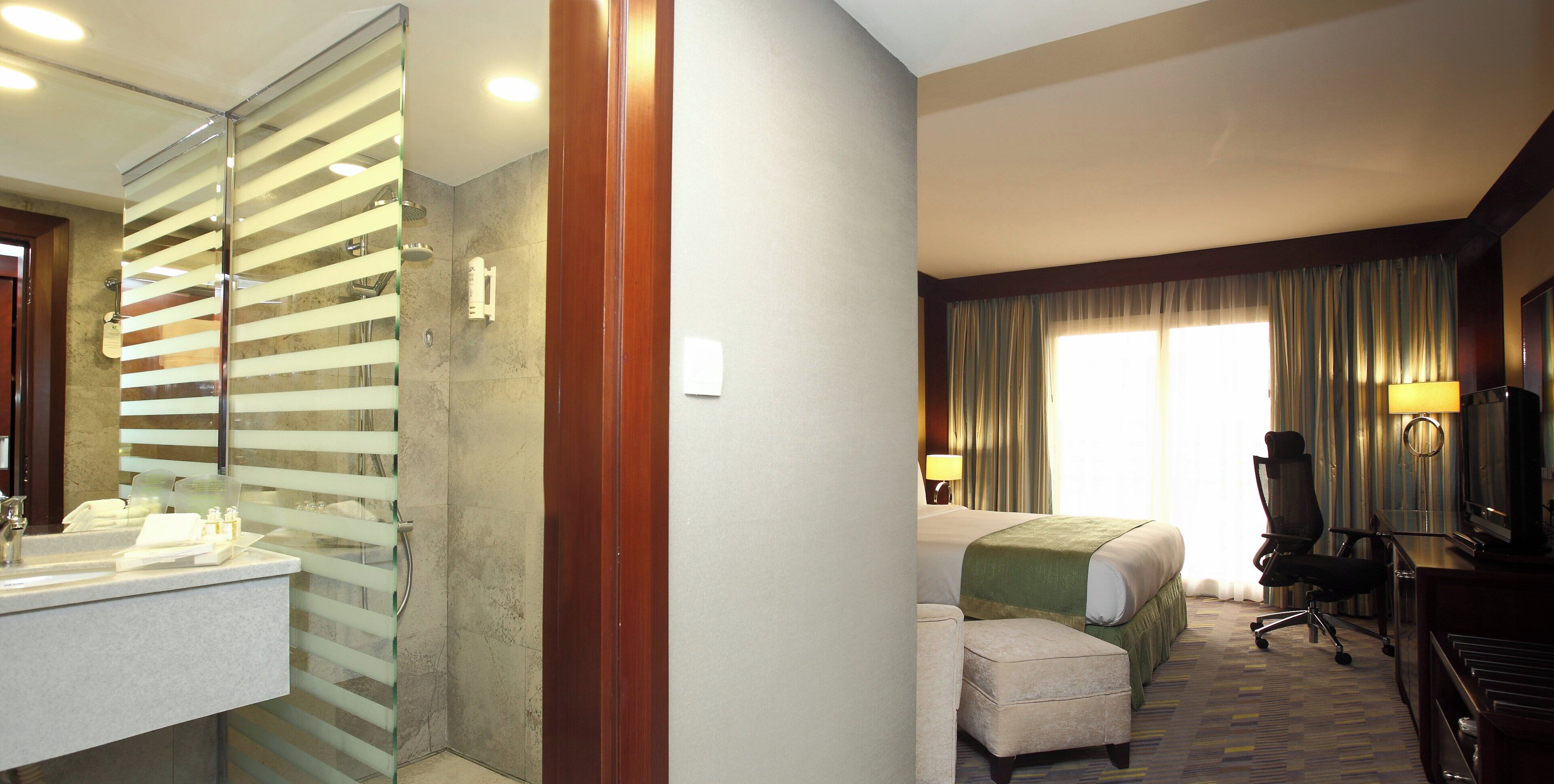 A hotel room with a bathroom, a bed, a desk, and a chair.