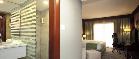 Una habitación de hotel con baño, cama, escritorio y silla.