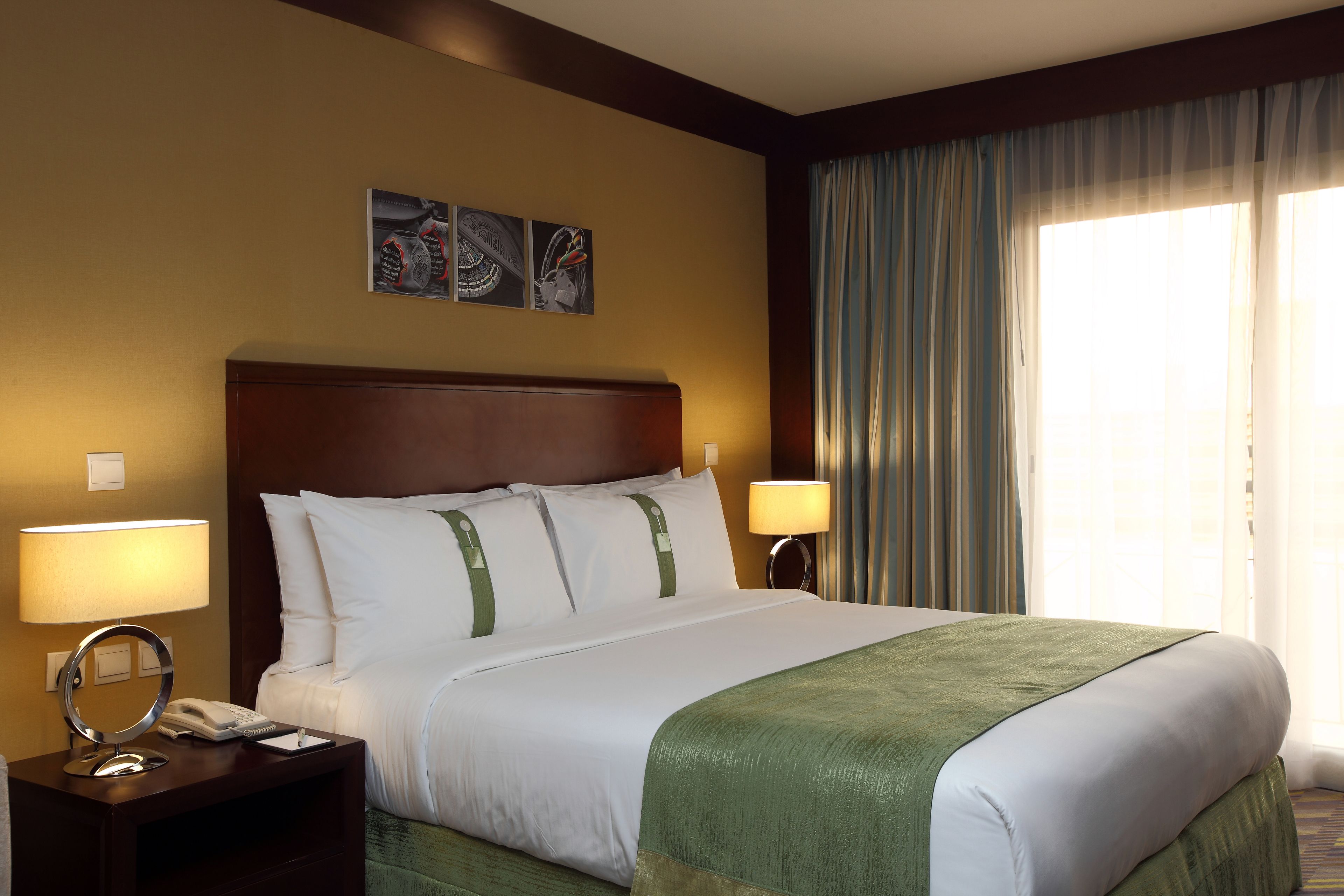 Habitación de hotel con una cama grande, dos lámparas de noche, una mesita de noche con teléfono y una obra de arte en la pared.