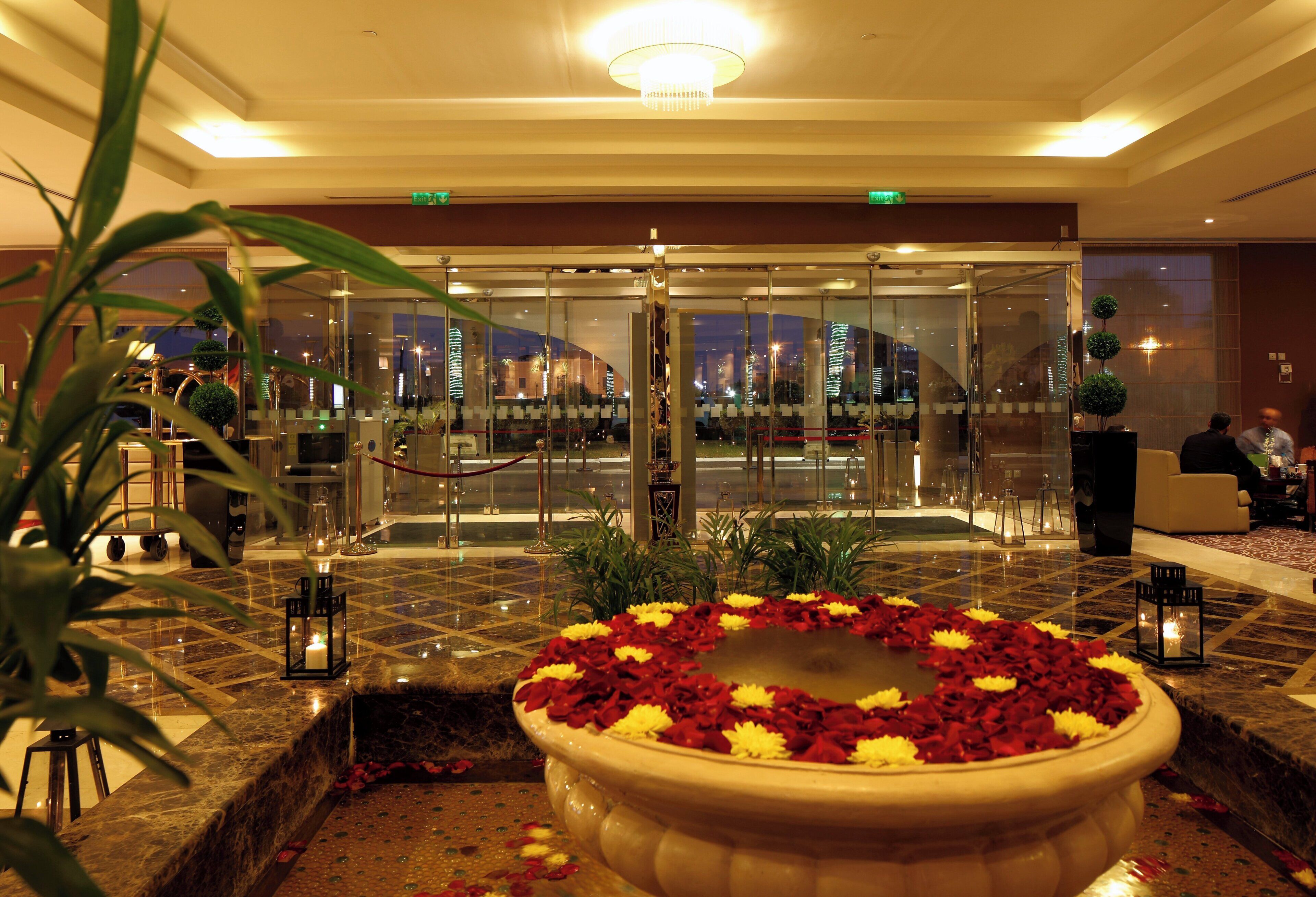 A hotel lobby with a reception desk, a glass entrance, and a decorative flower arrangement.