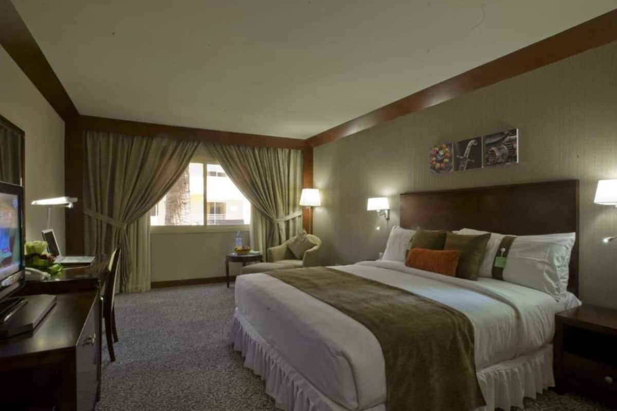 A hotel room with a large bed, a desk with a computer, a TV, and two bedside lamps.