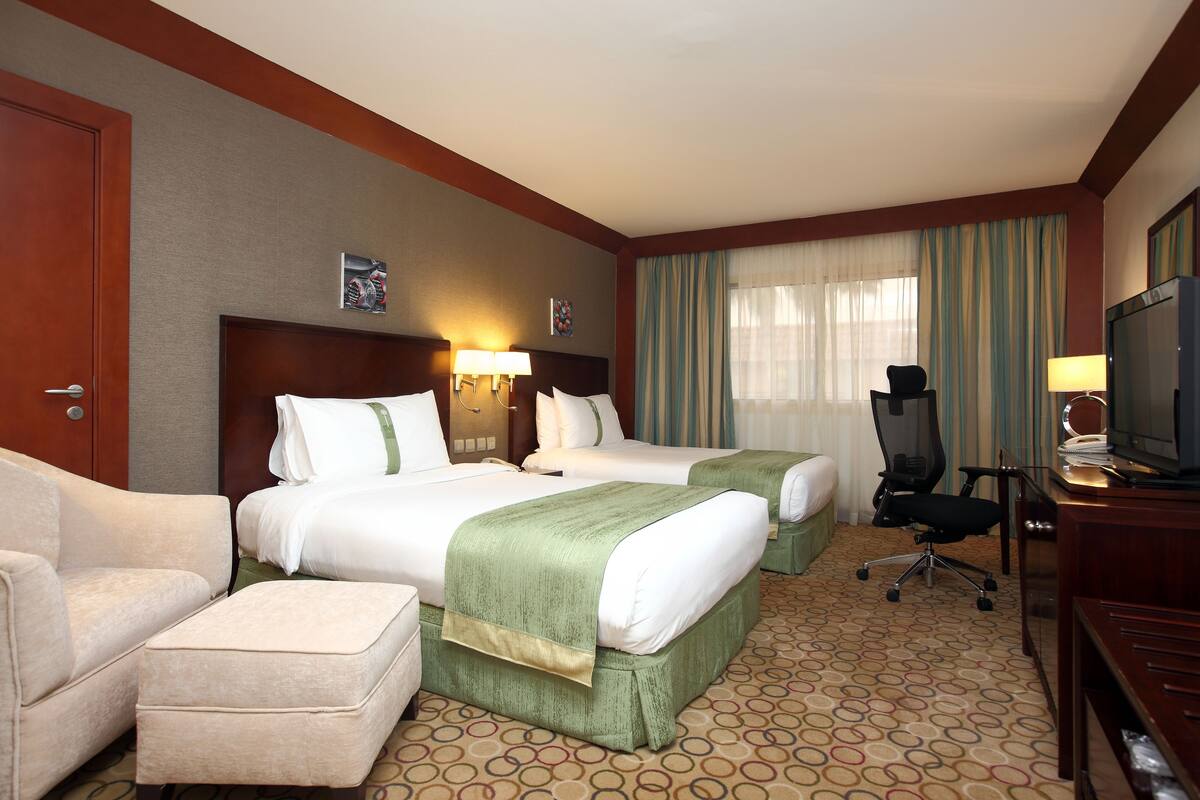 A hotel room with two beds, a desk, a TV, and a chair.