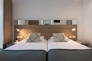 Una cama doble con dos almohadas, una mesita de noche con lámpara y un televisor montado en la pared.