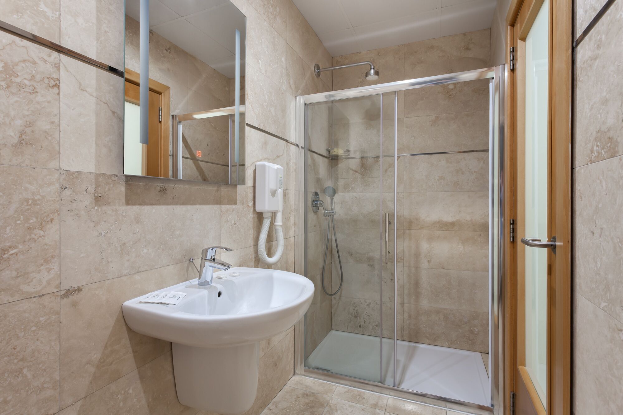 A bathroom with a glass shower enclosure, a white sink, and a mirror.
