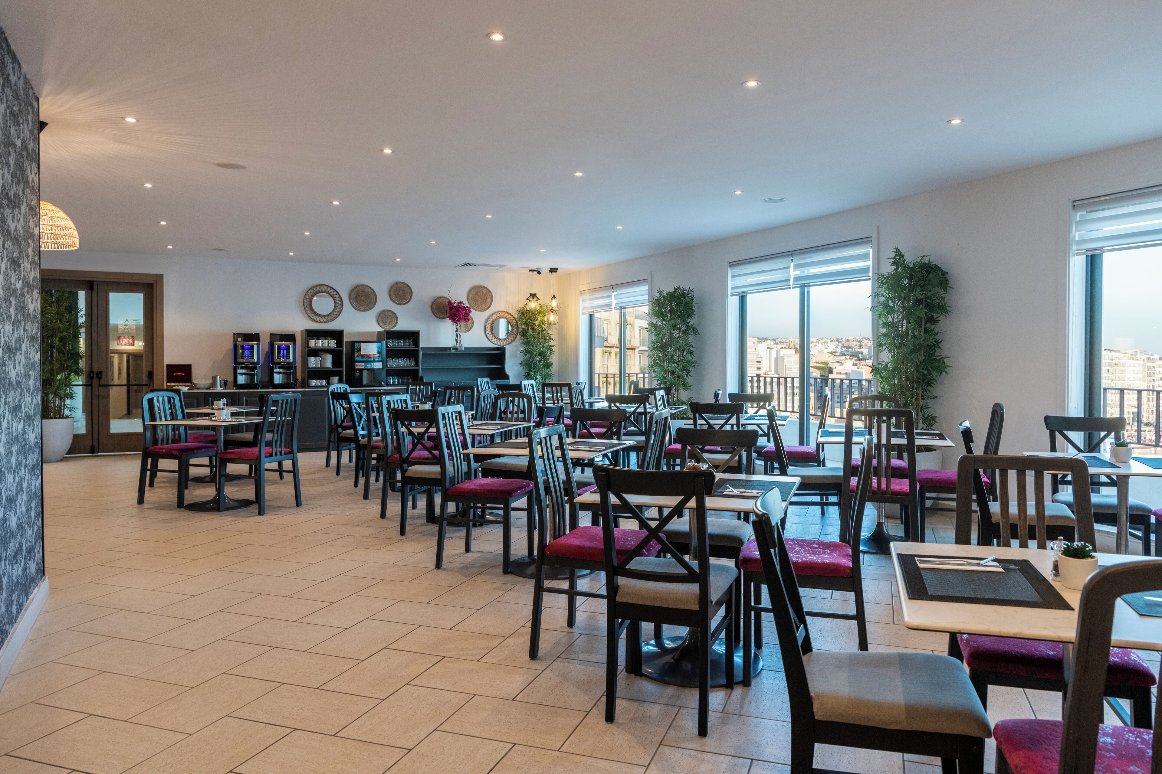 Een ruim restaurant met meerdere tafels en stoelen, grote ramen met uitzicht op de stad, en een modern interieur.