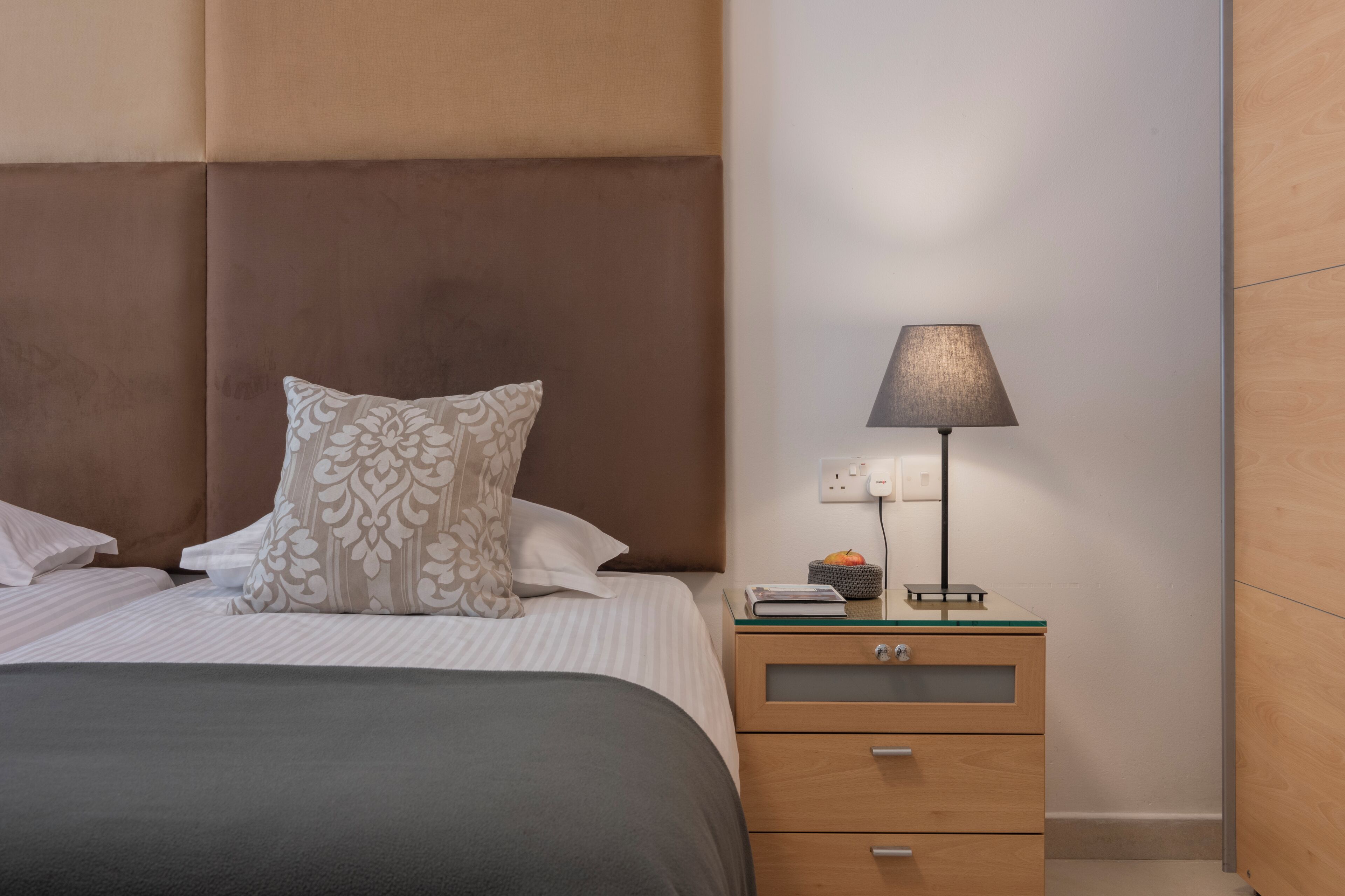 A neatly arranged bedroom with a bed, pillows, a bedside table with a lamp, and a drawer unit.